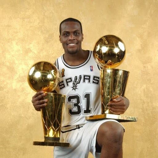 Malik Rose posing with 2 NBA championship trophies.